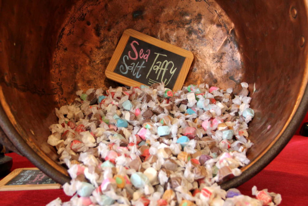 Wrapped sea salt taffy spilling from a large copper kettle beside a small chalkboard sign reading Sea Salt Taffy