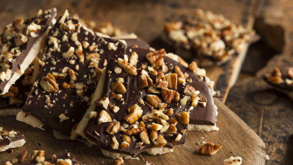 English toffee broken into uneven pieces, topped with chocolate and chopped nuts, resting on a wooden board