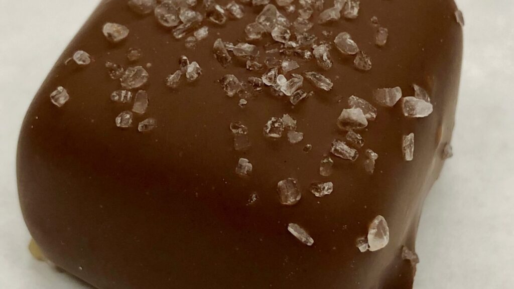 Close-up of a chocolate-dipped sea salt caramel topped with coarse salt crystals